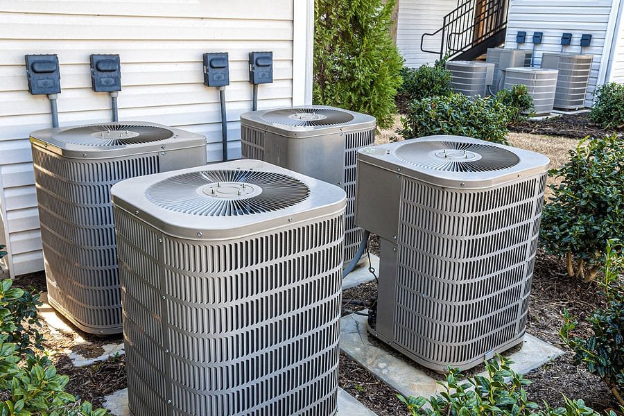 Three central air conditioning outdoor condenser units installed beside the wall of a home