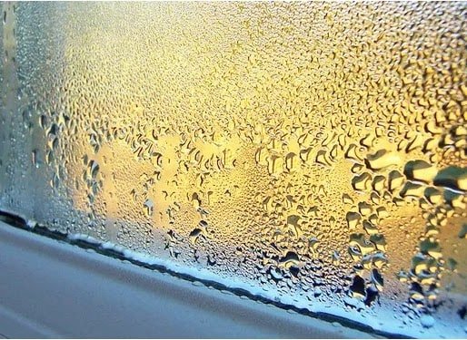 Water droplets of condensation on the inside of a window lit by warm light
