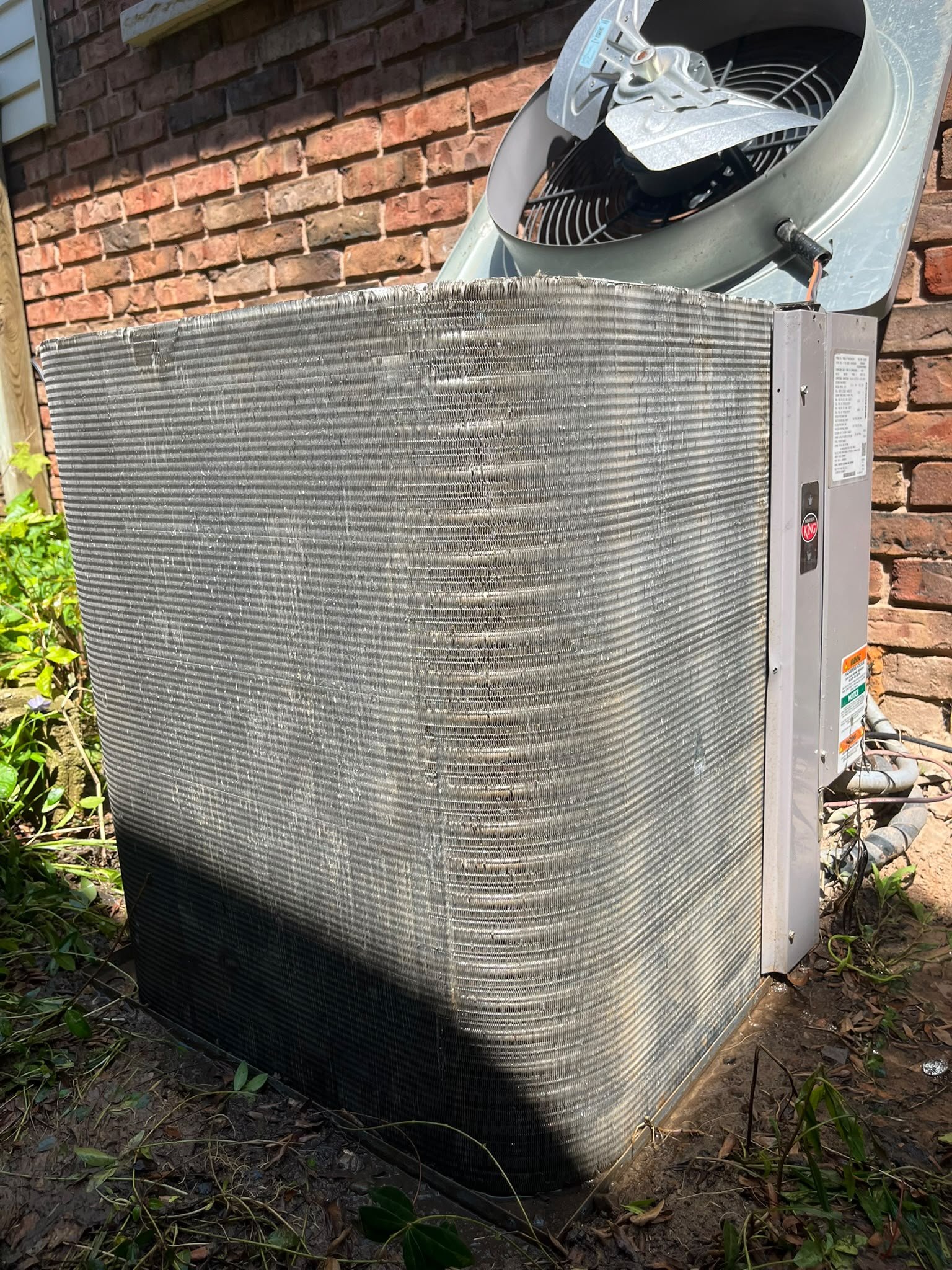 Air conditioner condenser coil with fins visible after the lint was removed, fan housing lifted off the top