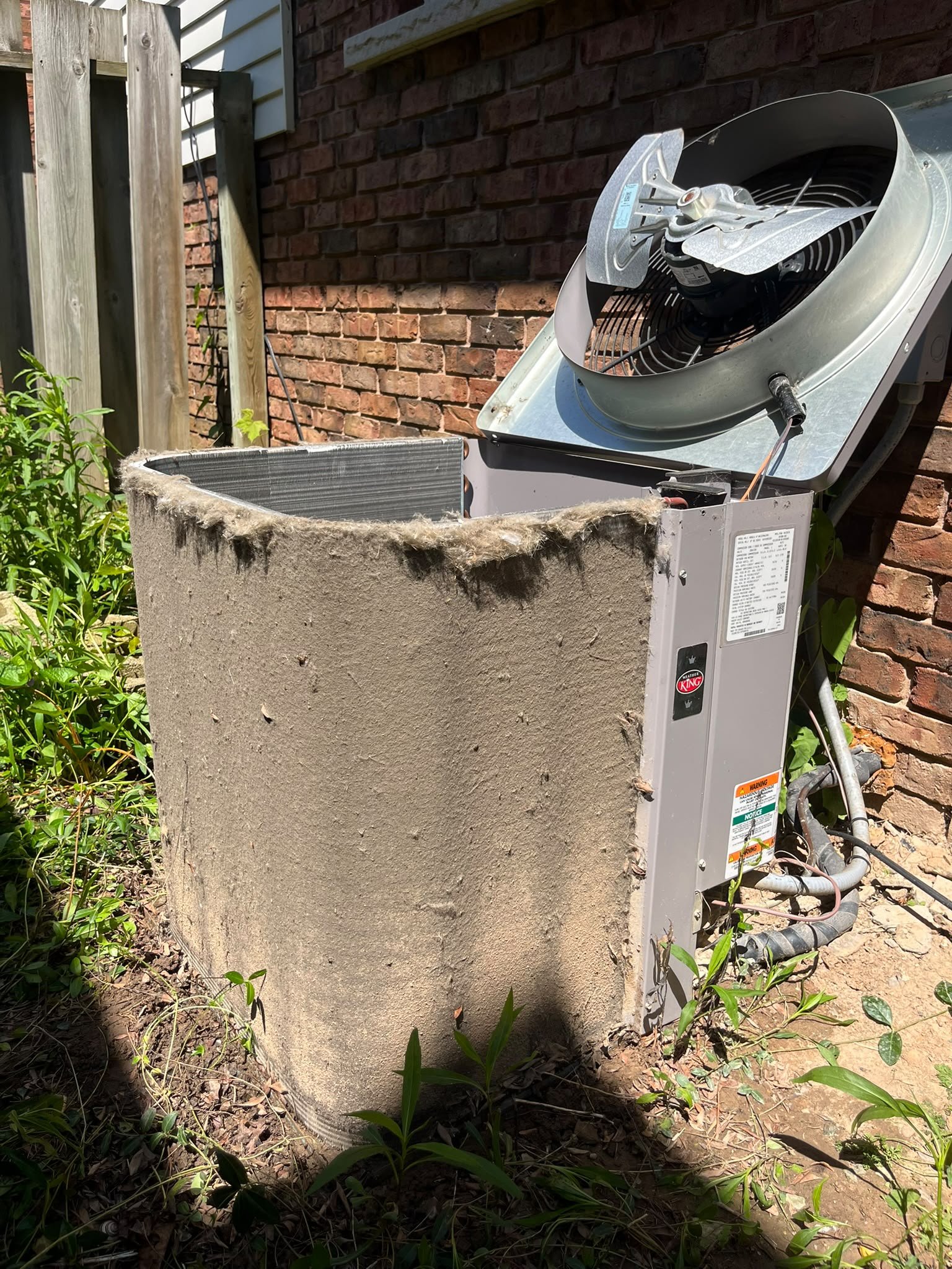 Air conditioner condenser cabinet side matted with a thick layer of lint and dirt before cleaning, with fluff hanging off the edge