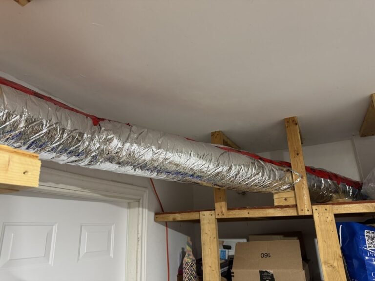 Silver insulated flexible duct running along a wood framed wall near a white door