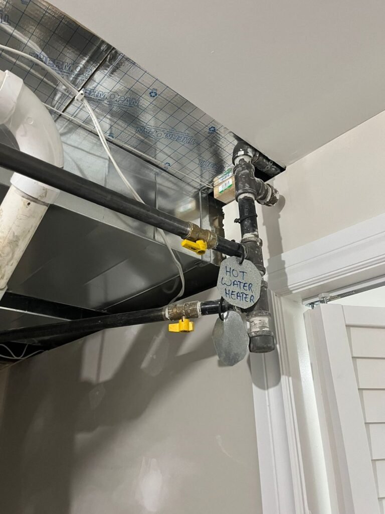 Hot water supply lines with yellow shut-off valves and a handwritten hot water tag near the ceiling of a utility room