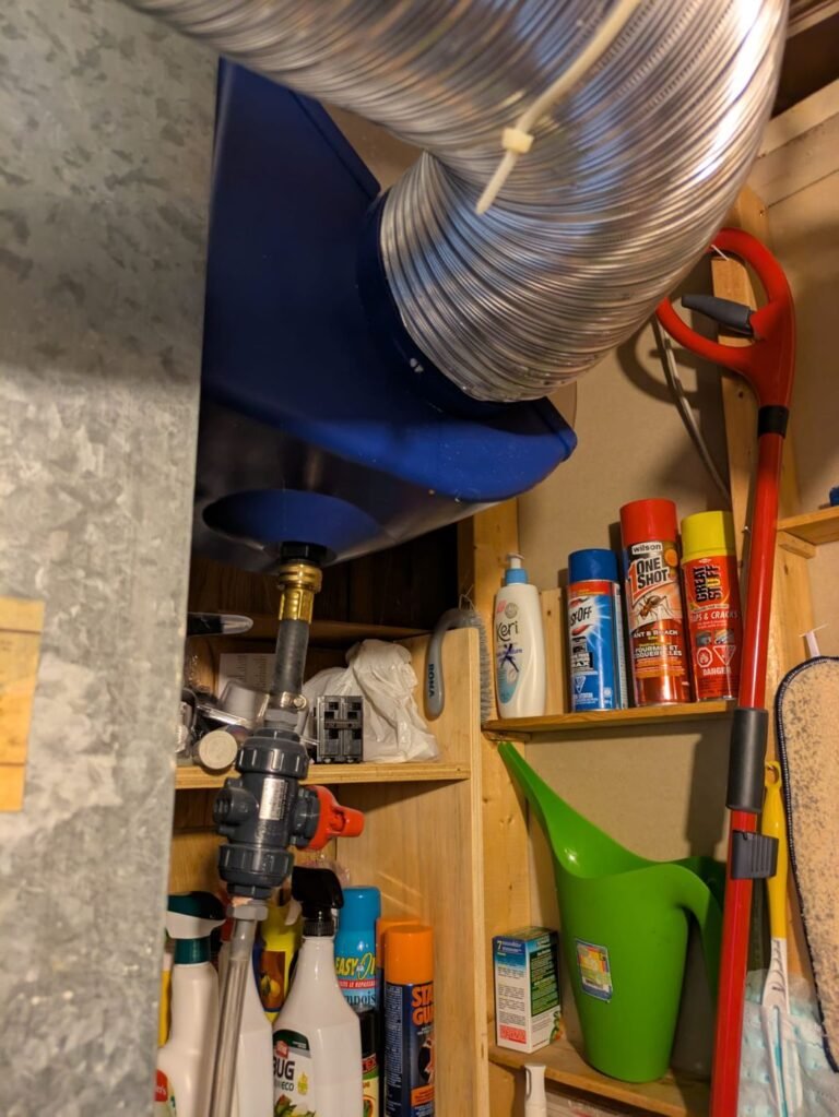 Blue humidifier housing with aluminum flex duct above a storage shelf and a water supply valve below it