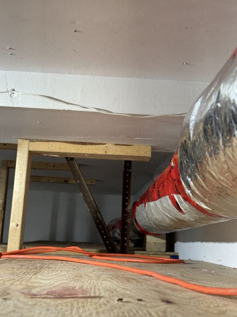 Insulated flexible duct wrapped with red tape run across the ceiling space of a tight crawlspace