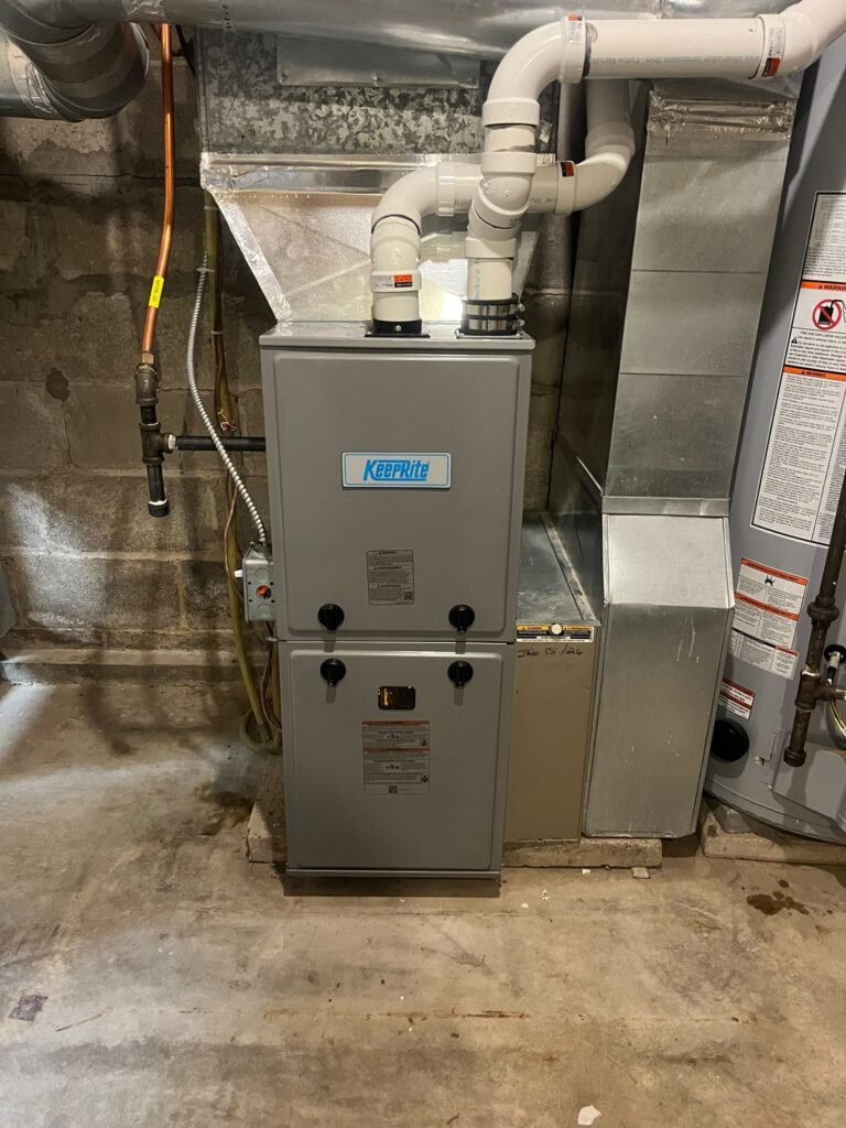 New KeepRite high-efficiency gas furnace in a basement with white PVC intake and exhaust pipes and a duct plenum on top