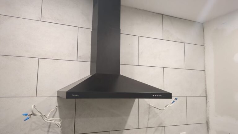 Black wall-mounted chimney range hood installed above a tiled kitchen wall with the wiring ready to connect