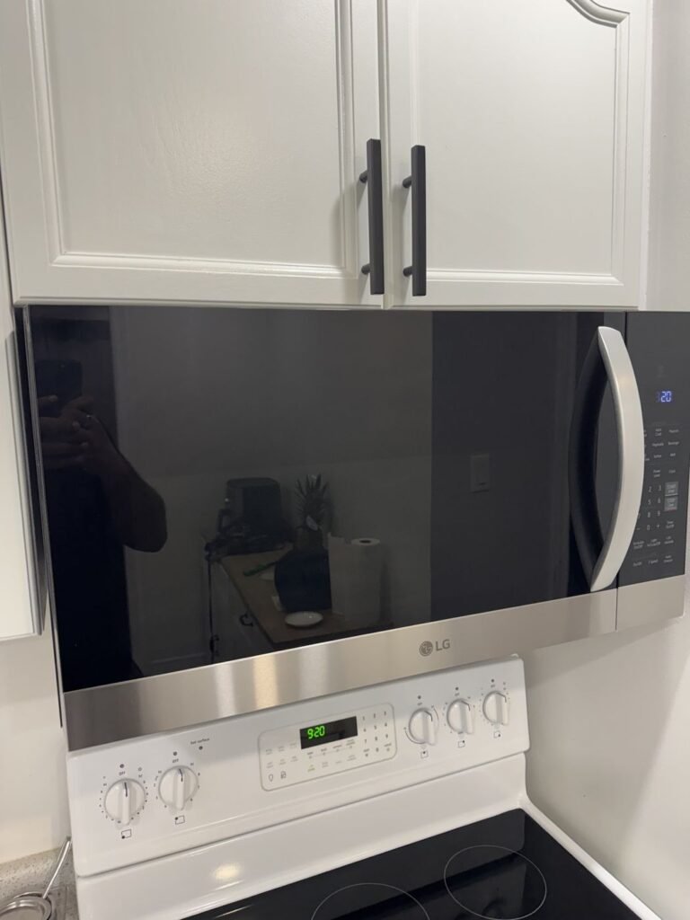 Stainless steel over-the-range microwave installed above a white electric range under white kitchen cabinets