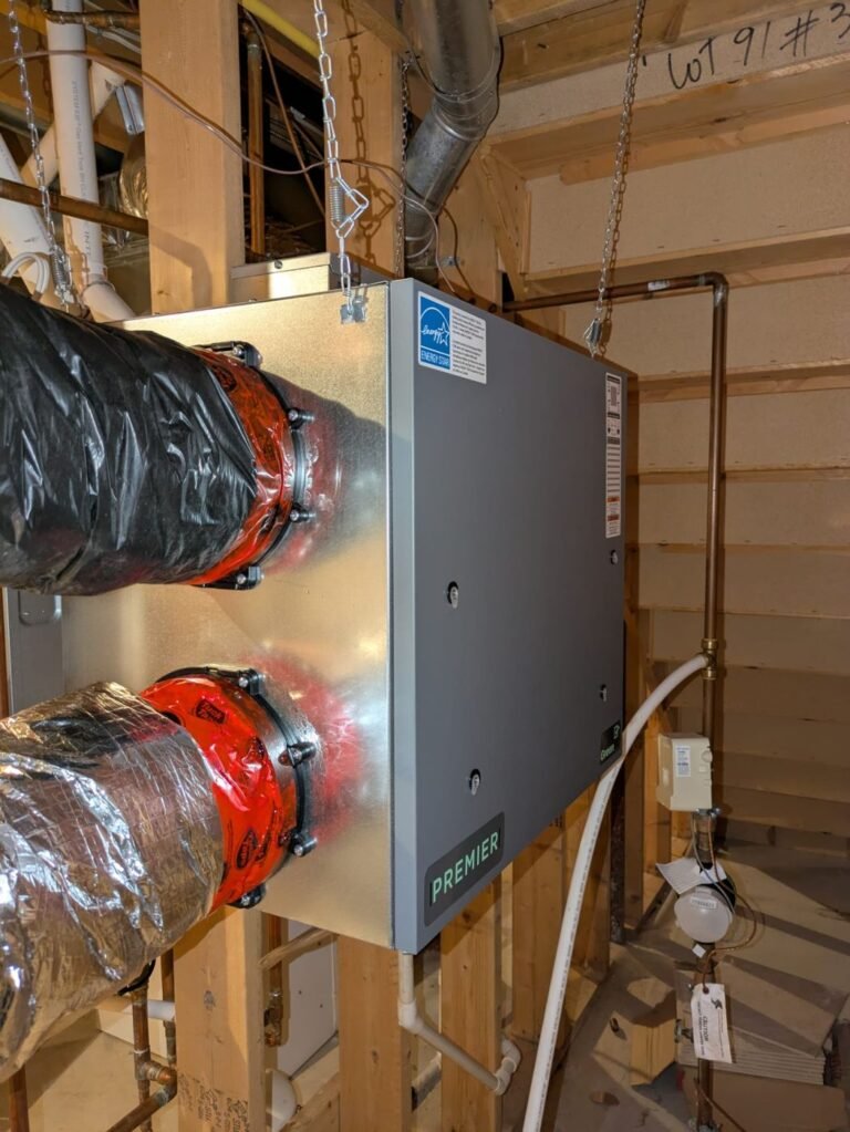 Silver ventilation unit with PREMIER label connected to two insulated flexible ducts with red and black wrap in an open stud wall