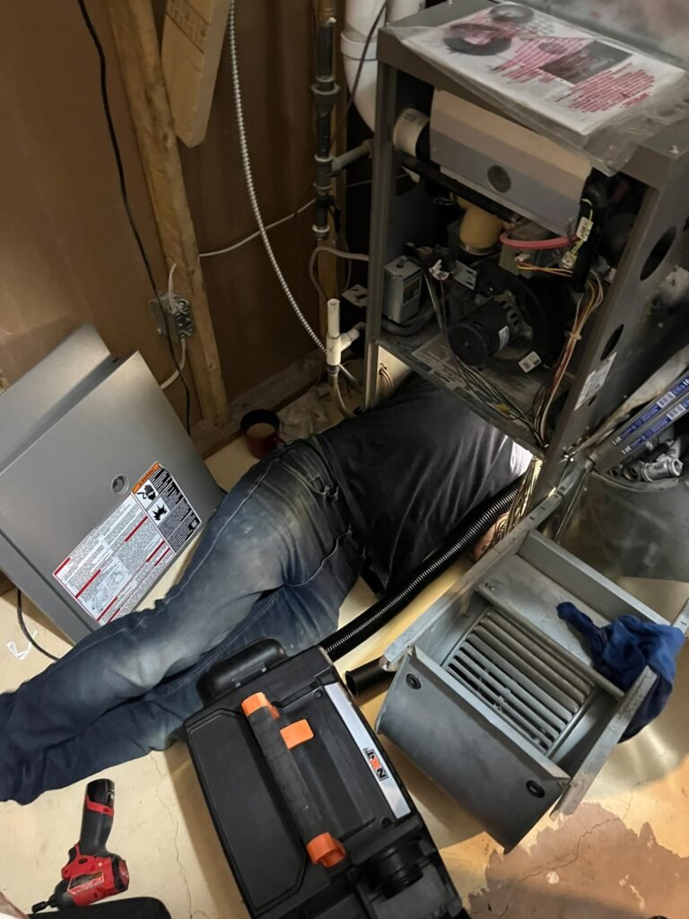 Technician lying on the floor with head and shoulders inside a furnace cabinet to repair the blower, tools and vacuum on the floor
