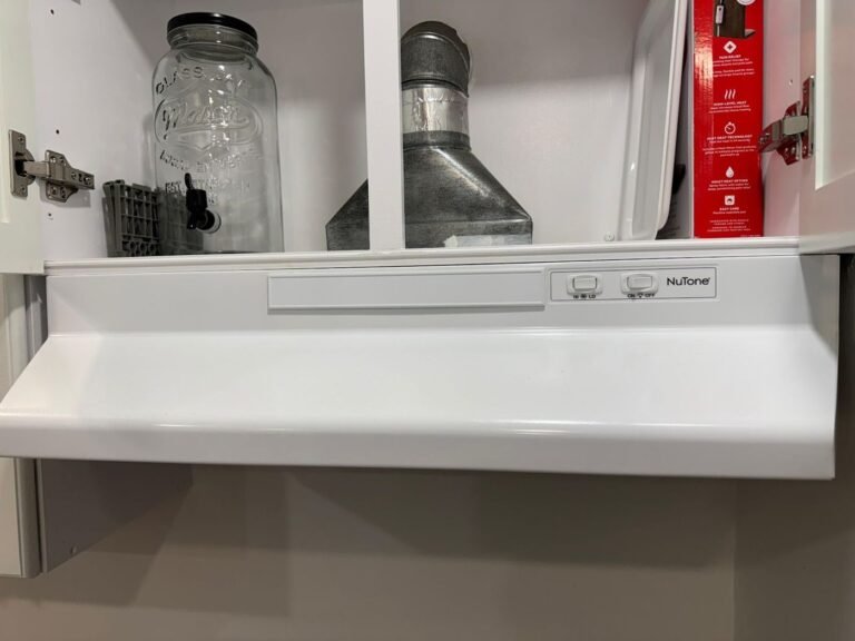 White under-cabinet range hood with a metal duct visible above it in a kitchen